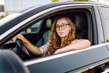 Güzel bir kadın araba kullanıyor, gezintiden zevk alıyor. Gün batımında gözlüklü genç bayan sürücü. Ulaşım ve eğlence kavramı.