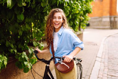 Şık giyinmiş genç bir kadın şehir caddesinde bisiklet sürüyor. Güzel bir turist aktif dinlenmenin tadını çıkarıyor. Yaşam tarzı, eğlenceli konsept.
