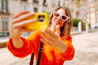 Güneşli bir günde selfie çeken mutlu bir turist. Günbatımı yürüyüşünün tadını çıkaran genç bir kadın. Turizm, blog konsepti. Etkin yaşam biçimi.