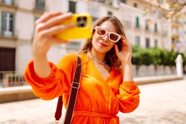 Güneşli bir günde selfie çeken mutlu bir turist. Günbatımı yürüyüşünün tadını çıkaran genç bir kadın. Turizm, blog konsepti. Etkin yaşam biçimi.