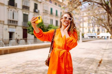 Güneşli bir günde selfie çeken mutlu bir turist. Günbatımı yürüyüşünün tadını çıkaran genç bir kadın. Turizm, blog konsepti. Etkin yaşam biçimi.