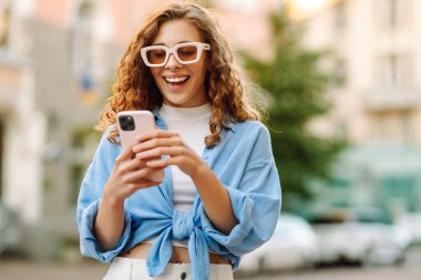 Gözlüklü ve telefonlu şık bir kadın şehirde eğleniyor. Genç bir kadın telefonda havanın ve mesajların tadını çıkarıyor. Turizm, güzellik konsepti.