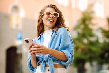 Gözlüklü ve telefonlu şık bir kadın şehirde eğleniyor. Genç bir kadın telefonda havanın ve mesajların tadını çıkarıyor. Turizm, güzellik konsepti.