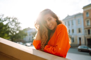 Parlak elbiseli güzel bir kadın gün batımında güzel bir binanın yanında poz veriyor. Mutlu kadın güneşin tadını çıkarıyor. Güzellik, moda ve eğlence konsepti.