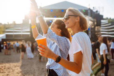 Bir plaj partisinde bira içip eğlenen mutlu bayan arkadaşlar. İki genç bayan arkadaş sahildeki bir müzik festivalinde tatilin tadını çıkarıyorlar. Arkadaşlık ve eğlence konsepti.