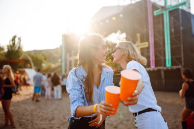 Bir plaj partisinde bira içip eğlenen mutlu bayan arkadaşlar. İki genç bayan arkadaş sahildeki bir müzik festivalinde tatilin tadını çıkarıyorlar. Arkadaşlık ve eğlence konsepti.