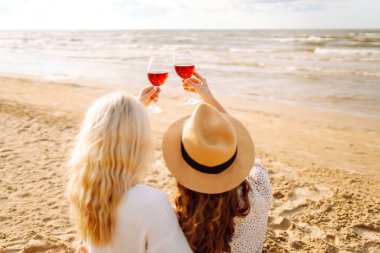 İki genç kadın sahilde bir bardakla oturuyor ve deniz manzarasının tadını çıkarıyorlar. Güzel kız arkadaşlar gün batımında eğleniyor ve birlikte vakit geçiriyorlar. Tatil ve hafta sonu konsepti.