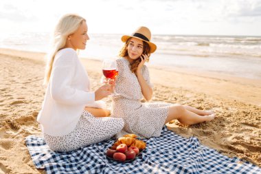 İki genç kadın sahilde bir bardakla oturuyor ve deniz manzarasının tadını çıkarıyorlar. Güzel kız arkadaşlar gün batımında eğleniyor ve birlikte vakit geçiriyorlar. Tatil ve hafta sonu konsepti.