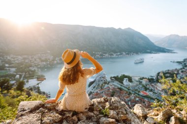 Bir kayanın üzerindeki genç bir kadın körfezin manzarasından hoşlanıyor. Şapkalı bir turist kendini özgür hisseder ve bacaklarını sallayarak gözlem güvertesinde eğlenir. Turizm, doğa ve güzellik kavramı.
