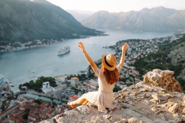 Bir kayanın üzerindeki genç bir kadın körfezin manzarasından hoşlanıyor. Şapkalı bir turist kendini özgür hisseder ve bacaklarını sallayarak gözlem güvertesinde eğlenir. Turizm, doğa ve güzellik kavramı.