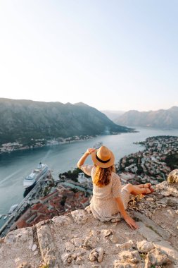 Bir kayanın üzerindeki genç bir kadın körfezin manzarasından hoşlanıyor. Şapkalı bir turist kendini özgür hisseder ve bacaklarını sallayarak gözlem güvertesinde eğlenir. Turizm, doğa ve güzellik kavramı.