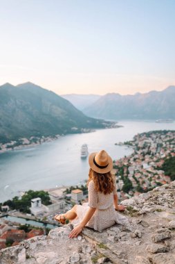 Bir kayanın üzerindeki genç bir kadın körfezin manzarasından hoşlanıyor. Şapkalı bir turist kendini özgür hisseder ve bacaklarını sallayarak gözlem güvertesinde eğlenir. Turizm, doğa ve güzellik kavramı.