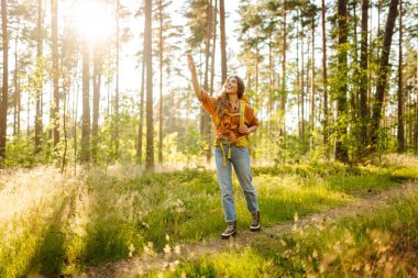 Sarı bir sırt çantasıyla genç bir bayan gezgin özgürlüğü hissediyor ve ormanda günbatımının tadını çıkarıyor. Güzel bir kadın eğleniyor ve yürüyüş parkurunda yürüyor. Yürüyüş ve özgürlük kavramı.
