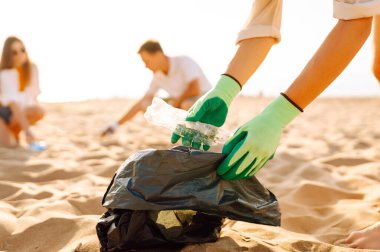 Genç arkadaşlar aktif olarak plaj temizliğine katılıyorlar. Neşeli gönüllüler gün batımında sahil boyunca plastik atık ve çöp topluyor. Ekoloji, ekoloji ve eğlence kavramı.