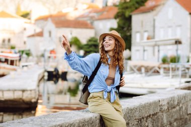 Şapkalı ve sırt çantalı güzel bir bayan gezgin gün batımında deniz manzarasının tadını çıkarıyor. Sırt çantalı genç bir kadın körfezin manzarasına hayran. Seyahat ve turizm konsepti. Etkin yaşam biçimi.