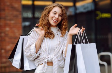 Alışveriş merkezinin dışındaki havanın tadını çıkaran neşeli bir kadın. Açık havadan alışveriş yapan genç bir turist. Aktif yaşam tarzı. İndirim ve tüketim kavramı.