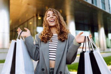 Günbatımında modern bir alışveriş merkezinin yakınında alışveriş torbalarıyla şık bir kadın. Alışverişten sonra yürüyüş yapan güzel bir kadın. Tüketim, tarz ve moda kavramı.