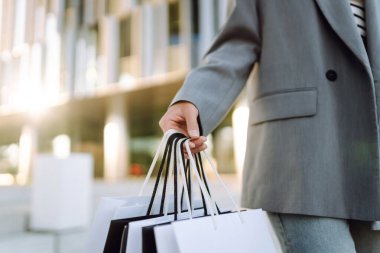 Günbatımında modern bir alışveriş merkezinin yakınında alışveriş torbalarıyla şık bir kadın. Alışverişten sonra yürüyüş yapan güzel bir kadın. Tüketim, tarz ve moda kavramı.