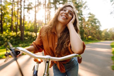 Güzel bir kadın güneşli bir parkta bisiklet sürerken selfie çeker. Genç bir kadın günbatımında bisiklet sürmekten hoşlanıyor. Etkin yaşam biçimi.