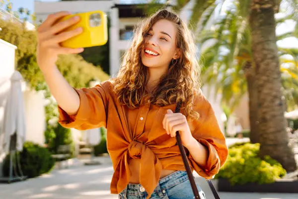 Şirin bir turist telefonuyla güneşli bir setin arka planına selfie çekiyor. Telefonu olan güzel bir kadın gün batımında yürüyüş ve blog yapmaktan hoşlanıyor. Turizm, blog konsepti.
