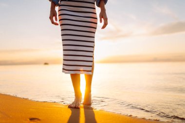 Gün batımında kumlu bir sahilde yürüyen genç bir kadının bacaklarının yakın çekimi. Güzel bir kadın sahilde yürürken günbatımının tadını çıkarıyor. Özgürlük kavramı.