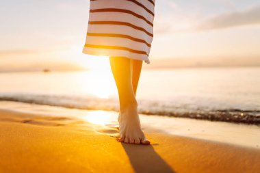 Gün batımında kumlu bir sahilde yürüyen genç bir kadının bacaklarının yakın çekimi. Güzel bir kadın sahilde yürürken günbatımının tadını çıkarıyor. Özgürlük kavramı.