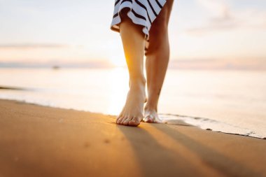 Gün batımında kumlu bir sahilde yürüyen genç bir kadının bacaklarının yakın çekimi. Güzel bir kadın sahilde yürürken günbatımının tadını çıkarıyor. Özgürlük kavramı.