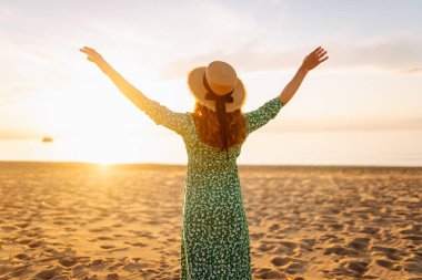Gün batımı kumsalında saman şapkalı mutlu bir kadının portresi. Elbiseli genç bir kadın deniz manzarasından zevk alıyor, özgürlüğü hissediyor. Etkin yaşam biçimi