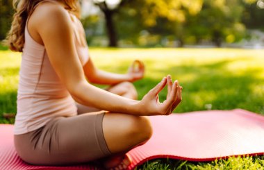 Genç bir kadın parkta minderle yoga yapıyor. Lotus pozisyonunda oturan zinde bir kadın günbatımında huzur ve sükunetin tadını çıkarıyor. Rahatlama kavramı.