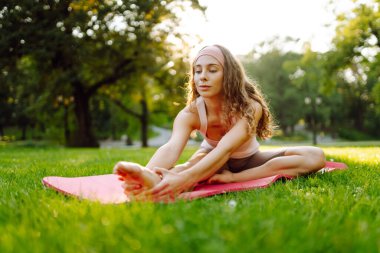 Genç bir kadın parkta minderle yoga yapıyor. Lotus pozisyonunda oturan zinde bir kadın günbatımında huzur ve sükunetin tadını çıkarıyor. Rahatlama kavramı.