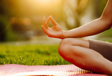 Genç bir kadın parkta minderle yoga yapıyor. Lotus pozisyonunda oturan zinde bir kadın günbatımında huzur ve sükunetin tadını çıkarıyor. Rahatlama kavramı.