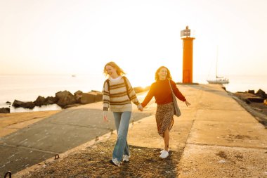 Kız arkadaşlar iskelede yürüyor ve gün batımında birlikte eğleniyorlar. İki genç kadın birlikte vakit geçiriyorlar, deniz manzarası ve yolculuğun tadını çıkarıyorlar. Arkadaşlık kavramı, eğlence..