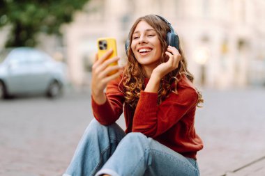 Telefonu ve kablosuz kulaklığı olan şık bir kadın güneşli sokaklarda müzik dinliyor. Genç bir turist dışarıda yürümekten hoşlanır. Teknoloji ve keyif kavramı.