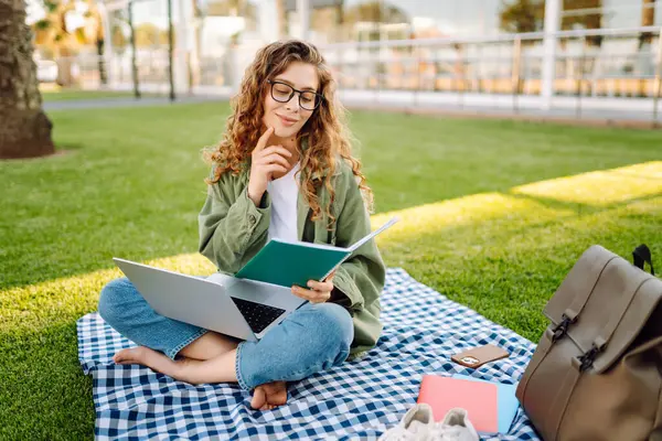 Güneşli bir parkta dizüstü bilgisayarı olan gözlüklü güzel bir kadın. Serbest çalışan bir kadın, dışarıda dizüstü bilgisayarla çalışıyor. Eğitim, uzak çalışma kavramı.