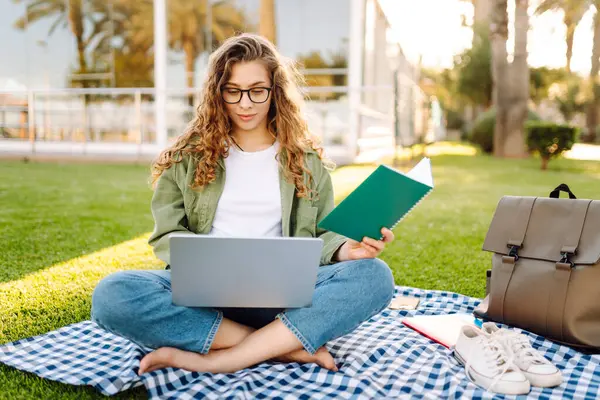 Güneşli bir parkta dizüstü bilgisayarı olan gözlüklü güzel bir kadın. Serbest çalışan bir kadın, dışarıda dizüstü bilgisayarla çalışıyor. Eğitim, uzak çalışma kavramı.