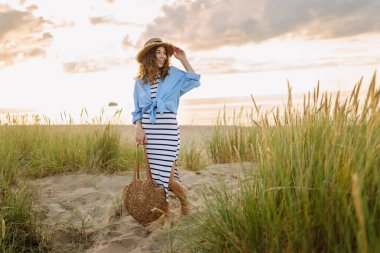 Hasır şapkalı neşeli kadın deniz kıyısında dinleniyor. Genç bir kadın sahilde gün batımının tadını çıkarıyor. Özgürlük, rahatlama, hafta sonu konsepti.