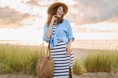 Hasır şapkalı neşeli kadın deniz kıyısında dinleniyor. Genç bir kadın sahilde gün batımının tadını çıkarıyor. Özgürlük, rahatlama, hafta sonu konsepti.