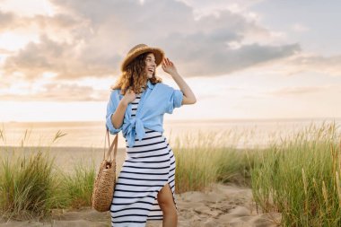 Hasır şapkalı neşeli kadın deniz kıyısında dinleniyor. Genç bir kadın sahilde gün batımının tadını çıkarıyor. Özgürlük, rahatlama, hafta sonu konsepti.