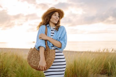 Hasır şapkalı neşeli kadın deniz kıyısında dinleniyor. Genç bir kadın sahilde gün batımının tadını çıkarıyor. Özgürlük, rahatlama, hafta sonu konsepti.