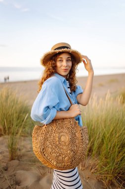 Hasır şapkalı neşeli kadın deniz kıyısında dinleniyor. Genç bir kadın sahilde gün batımının tadını çıkarıyor. Özgürlük, rahatlama, hafta sonu konsepti.