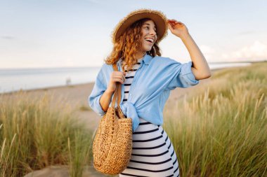 Hasır şapkalı neşeli kadın deniz kıyısında dinleniyor. Genç bir kadın sahilde gün batımının tadını çıkarıyor. Özgürlük, rahatlama, hafta sonu konsepti.