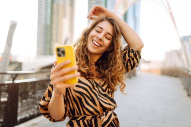 Şık giyinmiş, elinde telefonla Metropolis manzaralı selfie çeken mutlu bir kadın. Genç bir turist blogu yazıp dışarıda eğleniyor. Blogculuk, turizm konsepti.