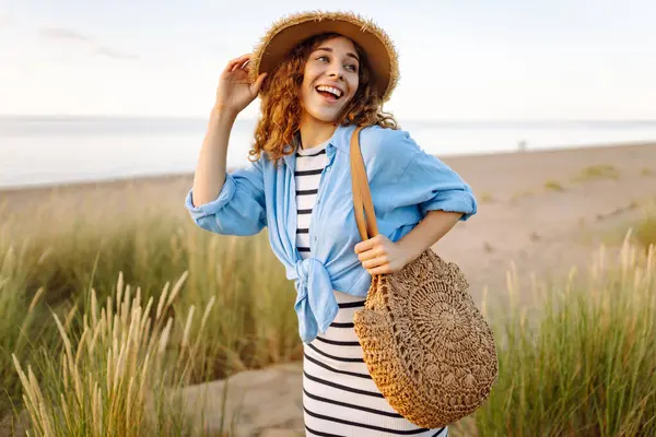 Hasır şapkalı neşeli kadın deniz kıyısında dinleniyor. Genç bir kadın sahilde gün batımının tadını çıkarıyor. Özgürlük, rahatlama, hafta sonu konsepti.