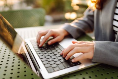 Dizüstü bilgisayarda günbatımı ışınlarıyla yazı yazan genç bir kadının elleri. Dışarıda dizüstü bilgisayarı olan serbest çalışan kadınların yakın çekimleri. İş, uzak çalışma konsepti.