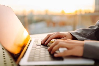 Dizüstü bilgisayarda günbatımı ışınlarıyla yazı yazan genç bir kadının elleri. Dışarıda dizüstü bilgisayarı olan serbest çalışan kadınların yakın çekimleri. İş, uzak çalışma konsepti.