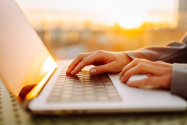 Dizüstü bilgisayarda günbatımı ışınlarıyla yazı yazan genç bir kadının elleri. Dışarıda dizüstü bilgisayarı olan serbest çalışan kadınların yakın çekimleri. İş, uzak çalışma konsepti.