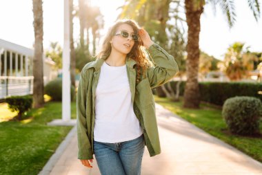 Güneşli şehir caddesinde gün batımında yürüyen güzel bir kadın. Sırt çantalı ve güneş gözlüklü mutlu turist dışarıda havanın tadını çıkarıyor. Hafta sonu ve eğlence konsepti.