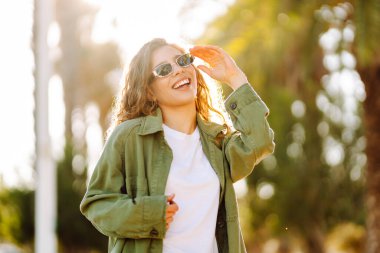 Güneşli şehir caddesinde gün batımında yürüyen güzel bir kadın. Sırt çantalı ve güneş gözlüklü mutlu turist dışarıda havanın tadını çıkarıyor. Hafta sonu ve eğlence konsepti.