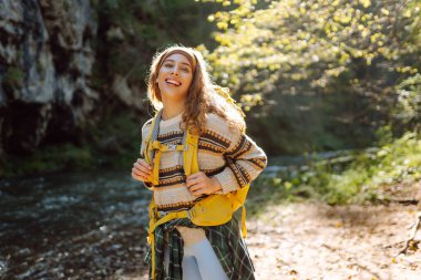 Sırt çantalı genç bir kadın dağ nehri yakınlarındaki dağ manzarasının tadını çıkarıyor. Mutlu kadın gezgin özgürlüğü hisseder, dağlarda yol boyunca yürür. Yürüyüş ve doğa konsepti.