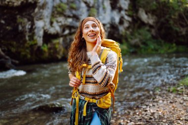 Sırt çantalı genç bir kadın dağ nehri yakınlarındaki dağ manzarasının tadını çıkarıyor. Mutlu kadın gezgin özgürlüğü hisseder, dağlarda yol boyunca yürür. Yürüyüş ve doğa konsepti.